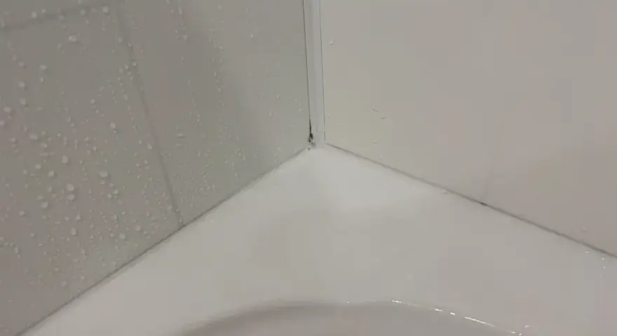 Angolo di una vasca da bagno con piastrelle bagnate e un sigillante bianco appena applicato per sigillare la vasca da bagno.
