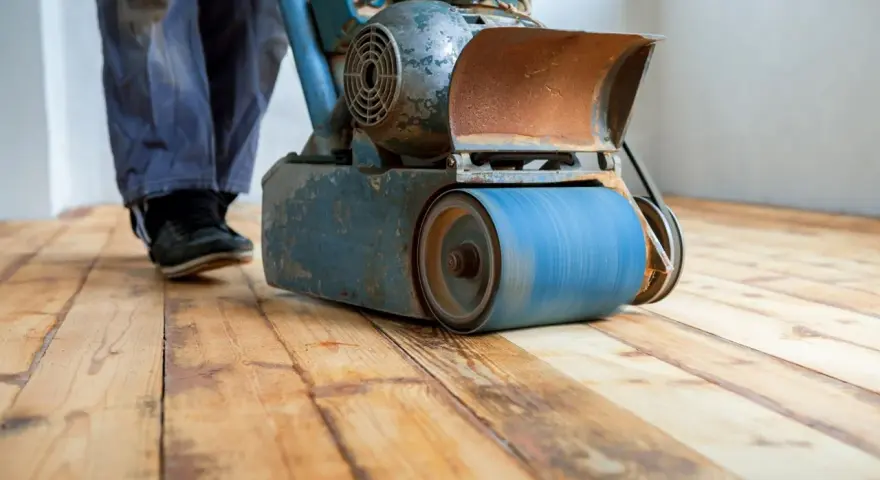 Levigatura parquet: un operaio usa una levigatrice per preparare il pavimento prima dell'imbiancatura. Il legno grezzo risplende sotto la macchina.