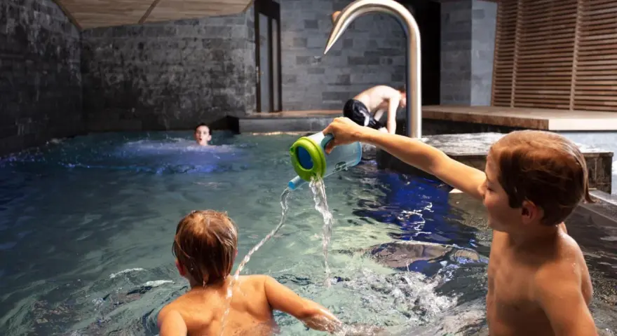 Bambini giocano in piscina, con un annaffiatoio. Nessuna indicazione su sauna età minima.
