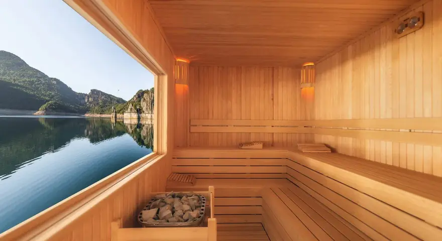 Interno di una sauna in legno con vista su un lago e montagne. Un luogo perfetto per capire cos'è una spa: relax e natura.