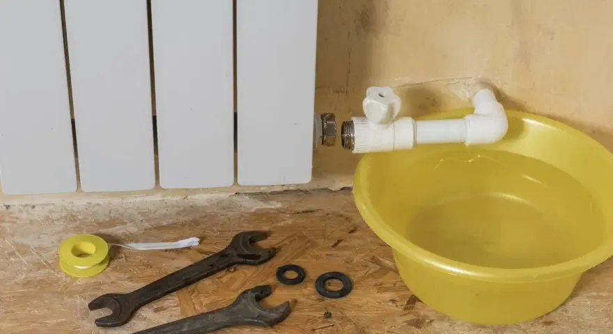 Riparazione di un termosifone che perde acqua e presenta ruggine. Attrezzi e bacinella gialla pronti per l'intervento.