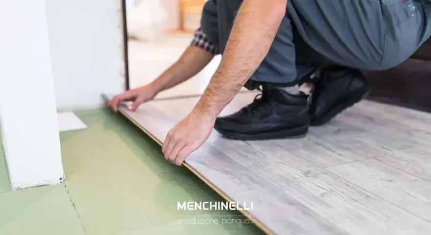Installazione di un parquet flottante con finitura effetto legno chiaro. Un artigiano posa le tavole con cura.