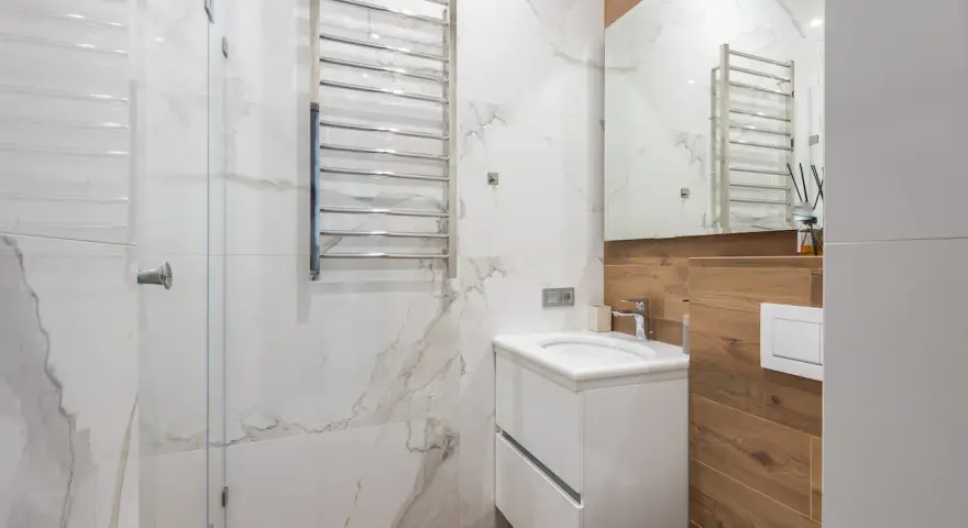 Bagno moderno con termoarredi cromati, lavabo sospeso e rivestimenti in marmo e legno.