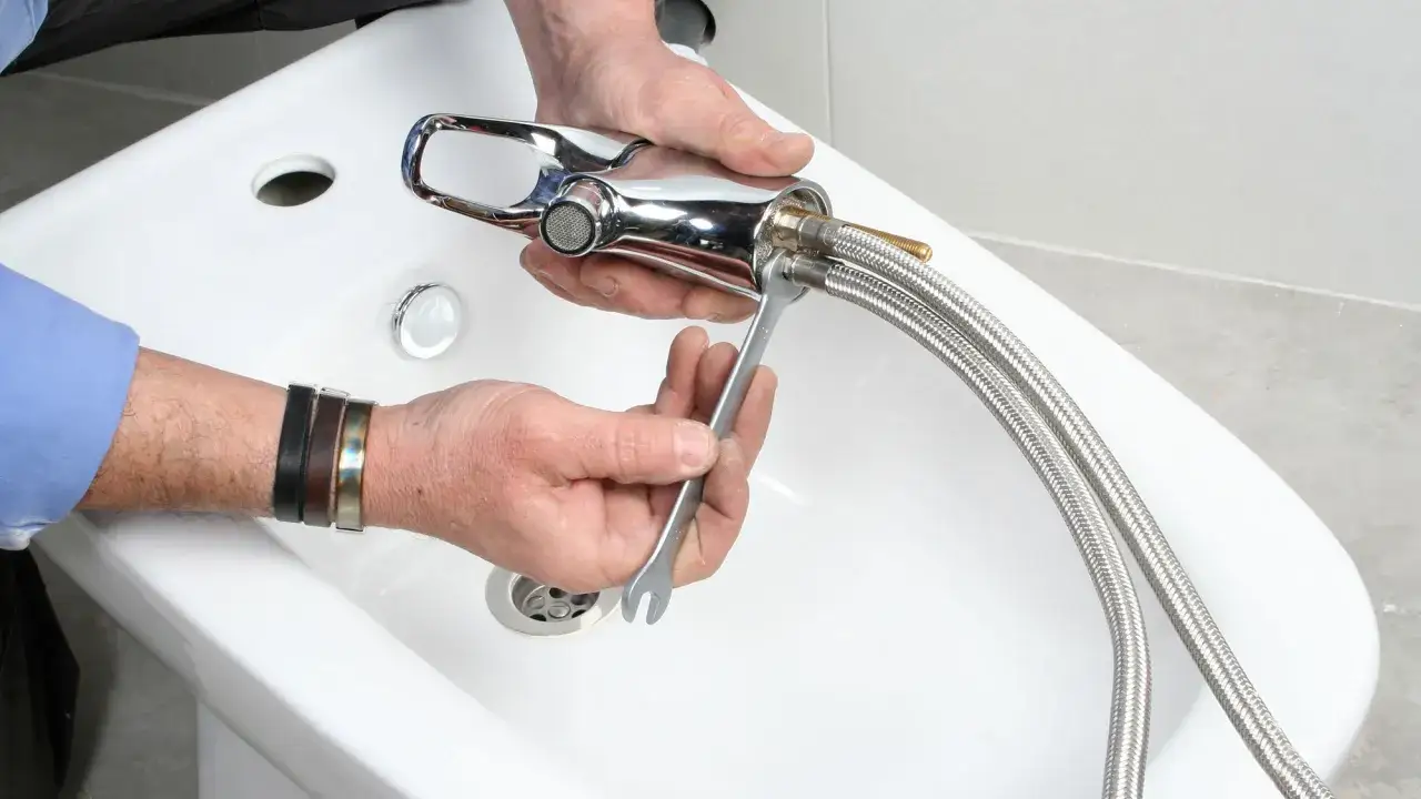 Mani esperte eseguono il montaggio rubinetto bidet, fissando i flessibili con una chiave inglese.