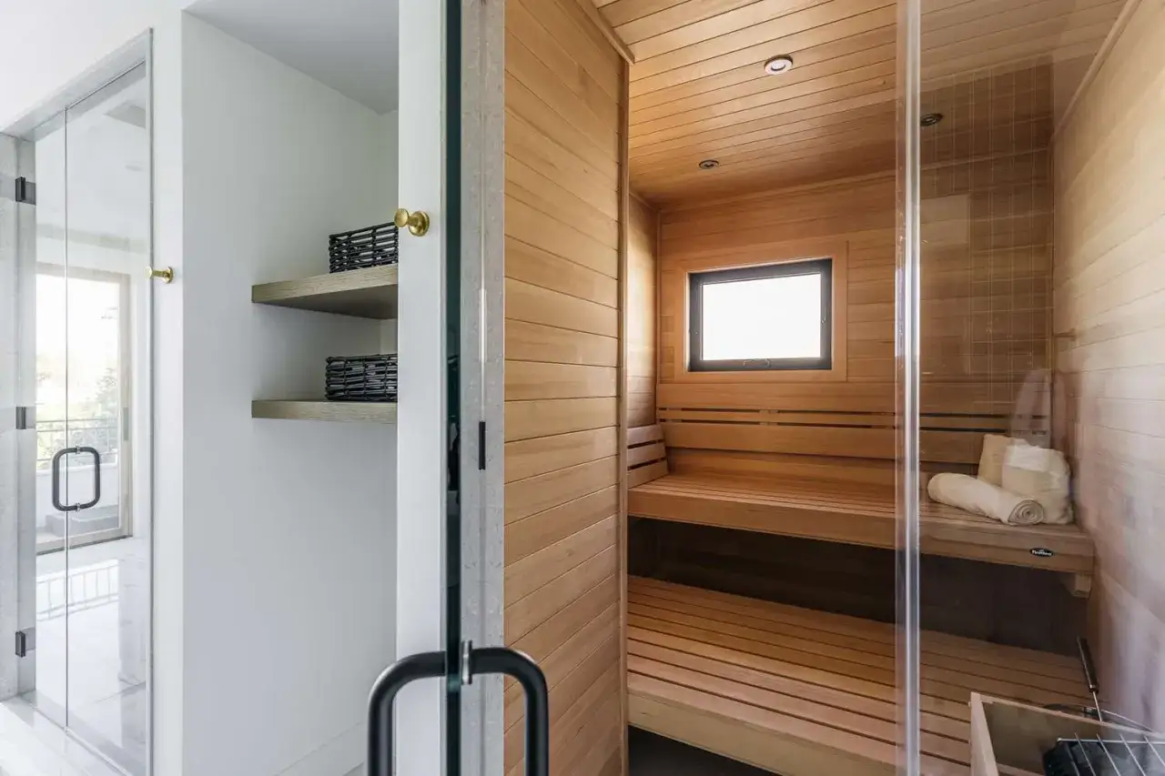 Interno di una spa moderna con sauna in legno, doccia in vetro e mensole.