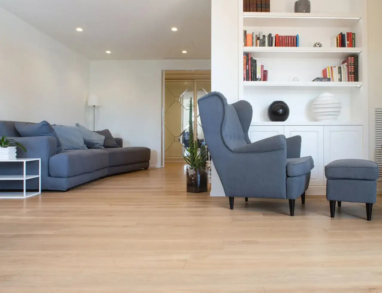 Soggiorno moderno con divano grigio, poltrona e pouf, su un luminoso parquet verniciato ad acqua. Ottime opinioni per questo pavimento naturale.