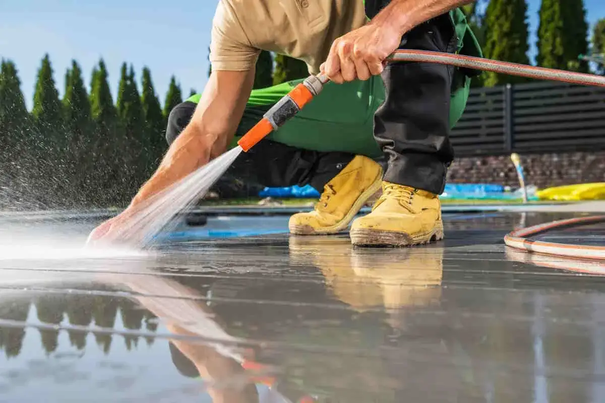 Uomo accovacciato pulisce pavimento esterno con idropulitrice, rimuovendo sporco e residui per un risultato impeccabile.