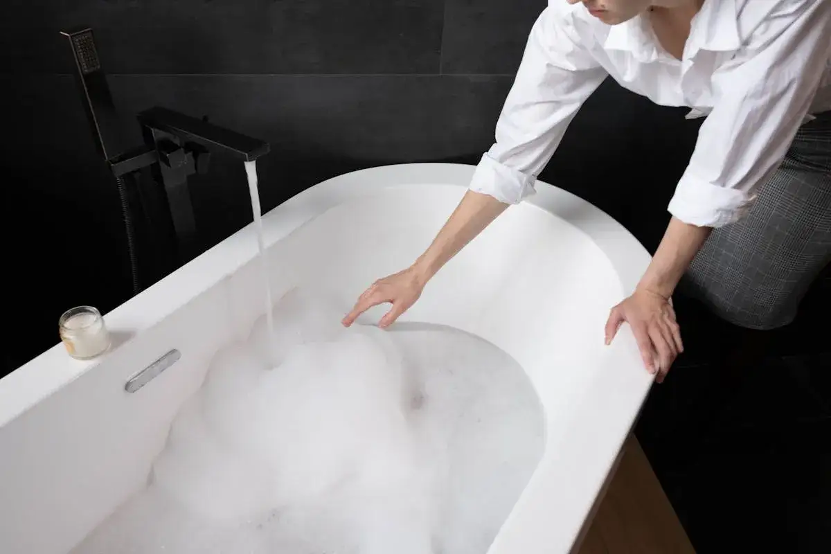 Donna con camicia bianca riempie la vasca da bagno con schiuma, un passo per come pulire la vasca da bagno.