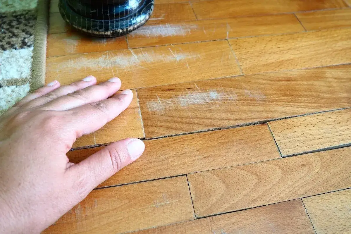 Mano su parquet rovinato, graffi e fessure evidenti. Si valuta come pulire parquet rovinato per un restauro.