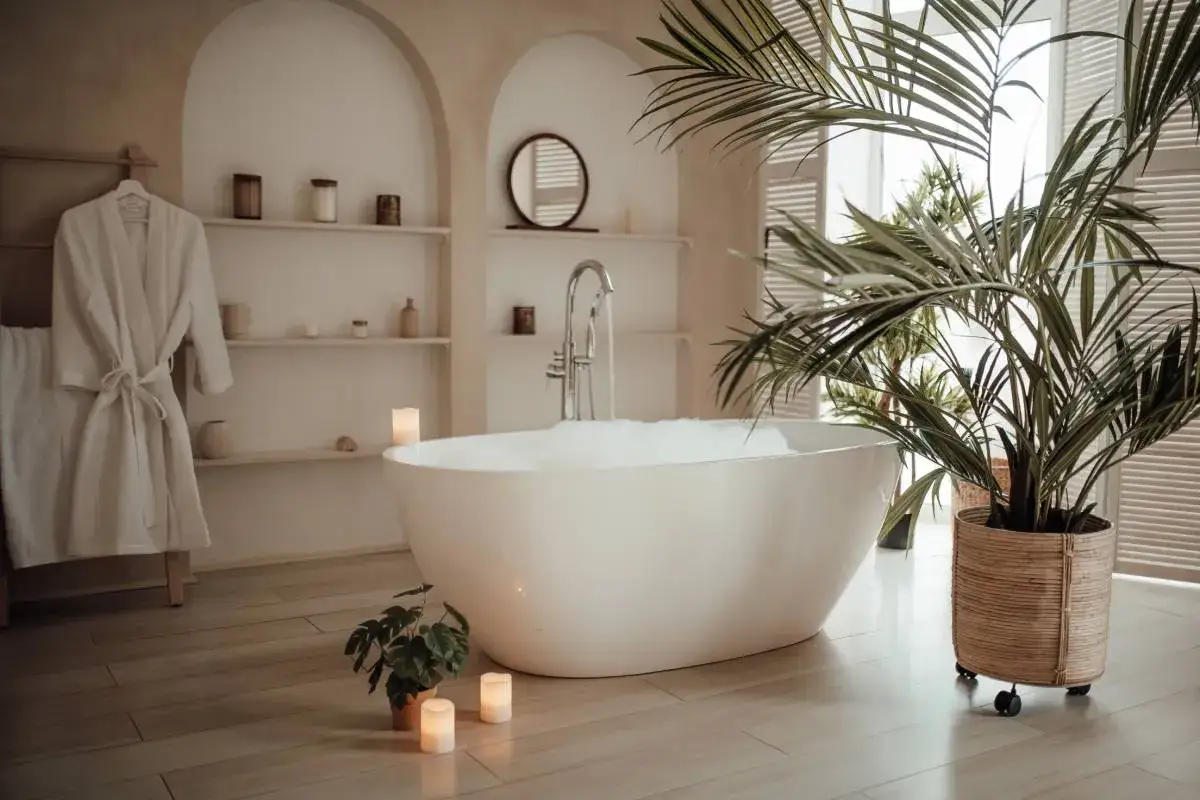 Bagno rilassante con vasca da bagno di lusso piena di schiuma, accappatoio bianco appeso, piante verdi e candele accese.