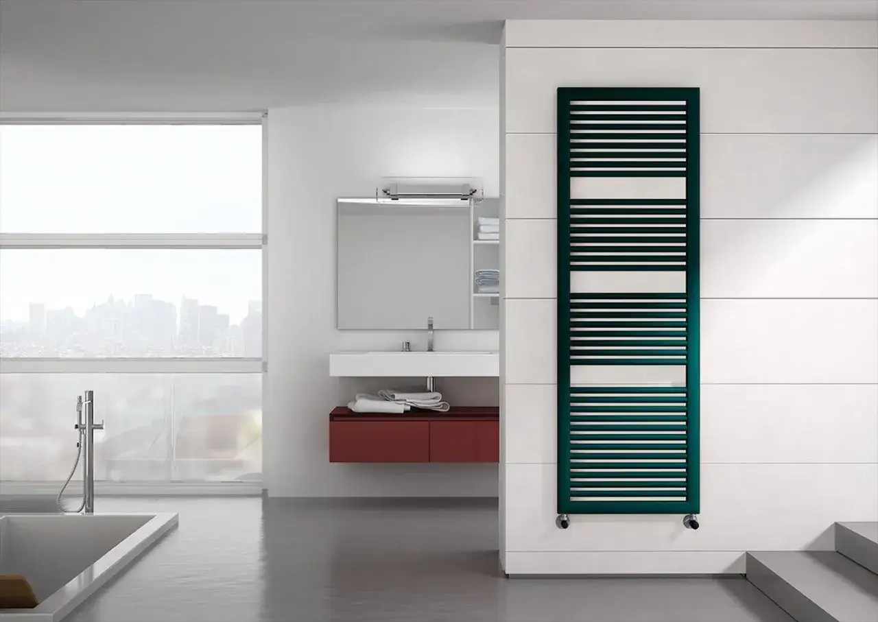Elegante termoarredo Irsap verde petrolio, con un design moderno a listelli orizzontali, si integra perfettamente in un bagno minimalista con vista sulla città.