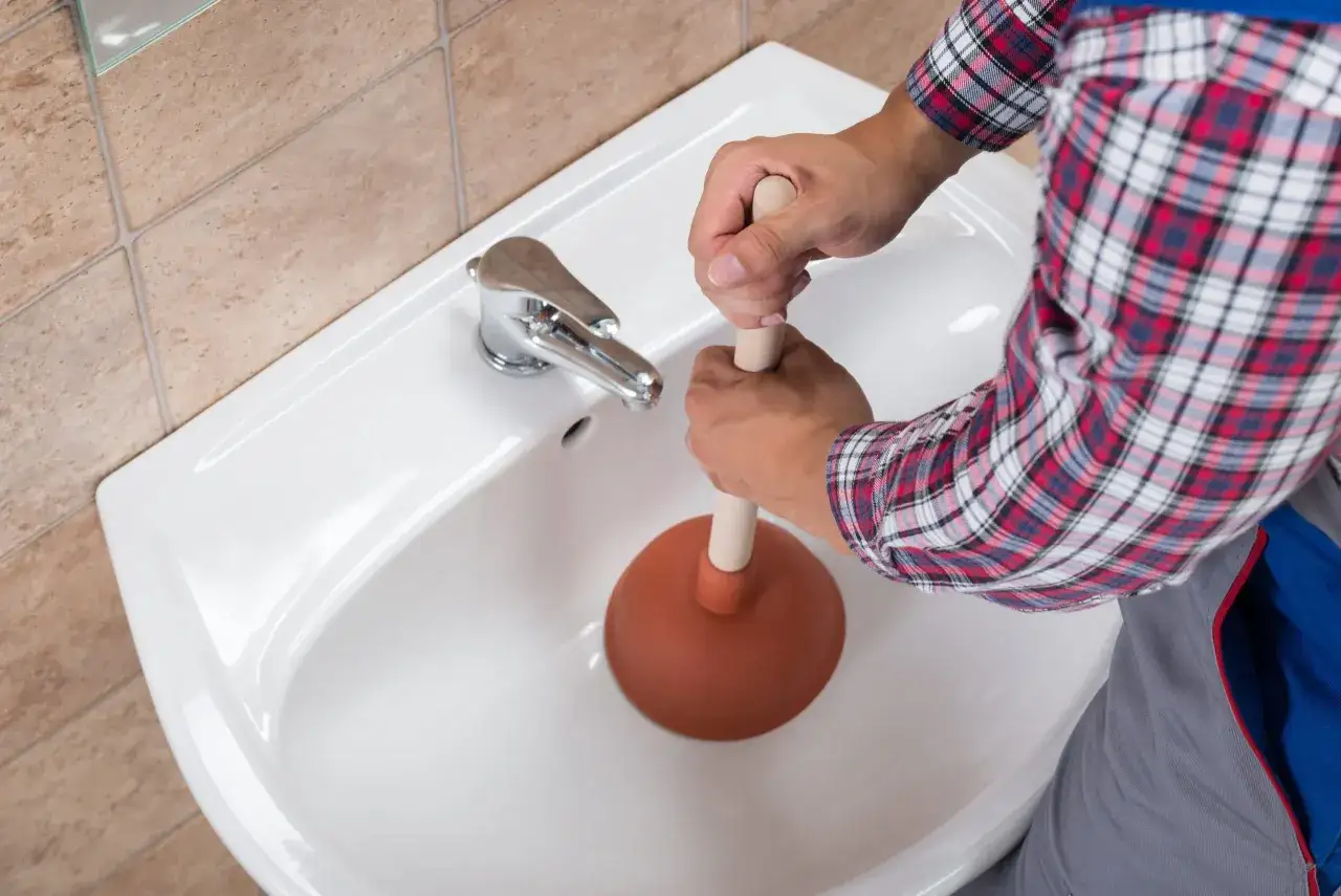 Mani che usano uno stantuffo per liberare un lavandino bagno otturato.