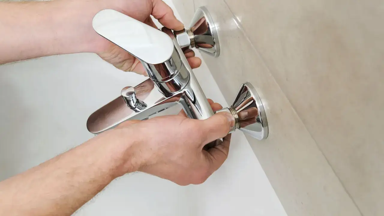 Mani che installano un nuovo miscelatore cromato per la vasca da bagno. Sostituzione miscelatore vasca da bagno in corso.