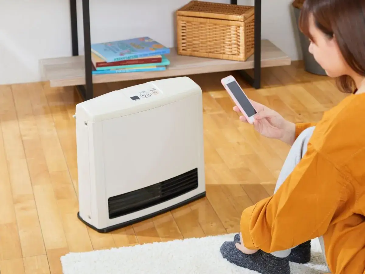 Donna controlla i sistemi di riscaldamento elettrici tramite smartphone, seduta sul tappeto accanto al calorifero.