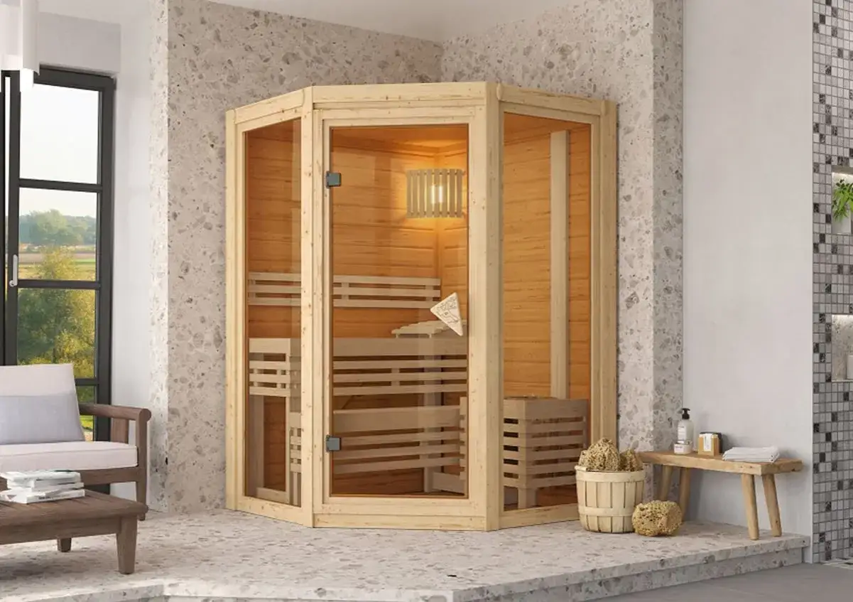 Angolo relax con sauna finlandese in legno e vetro, panchina, cesto con spugne naturali e vista su un giardino.