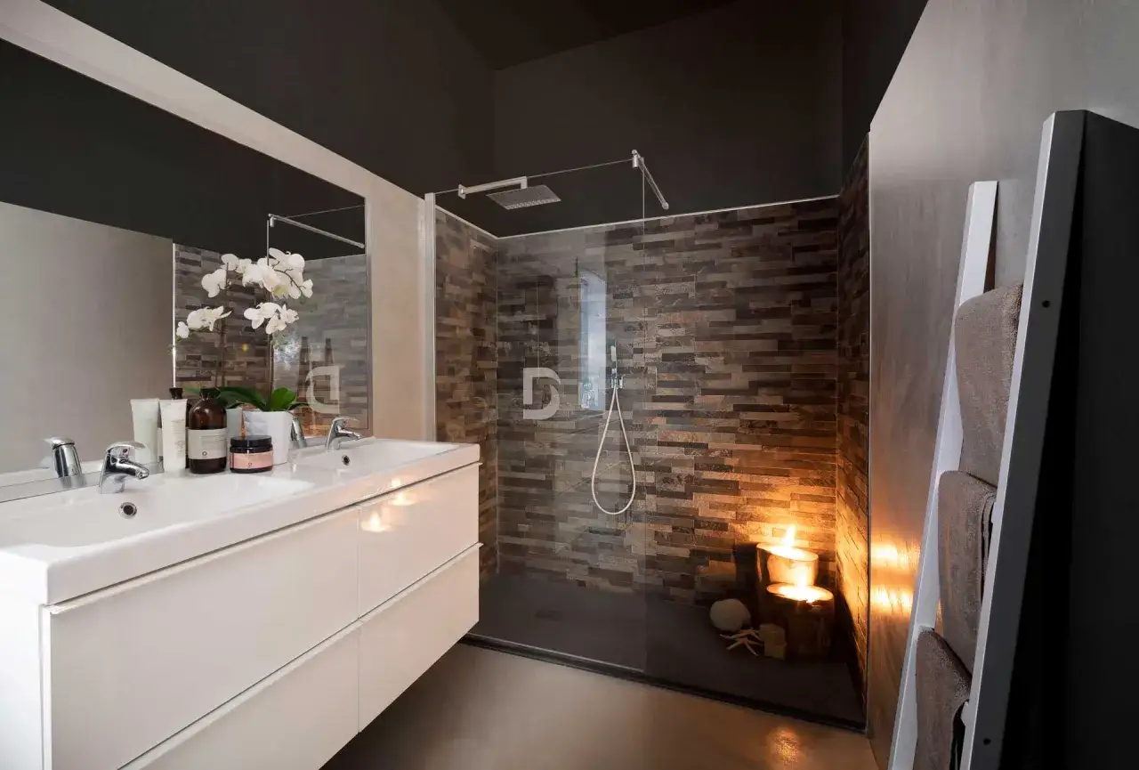 Bagno moderno con lavabo doppio, doccia a filo pavimento con parete in pietra e illuminazione soffusa. Soluzioni doccia senza box per un design minimalista.