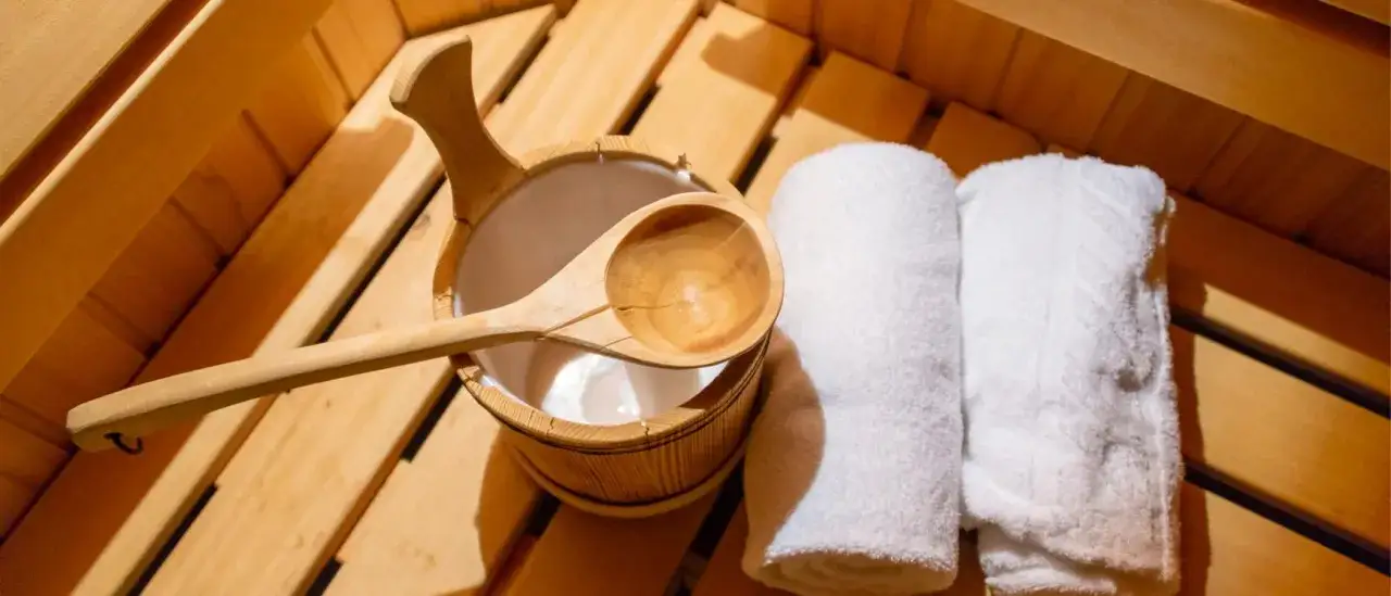 Secchiello e mestolo in legno, asciugamani bianchi arrotolati, pronti per un momento di relax. L'atmosfera è quella di una sauna, perfetta per chi cerca il benessere dei nudi in sauna.