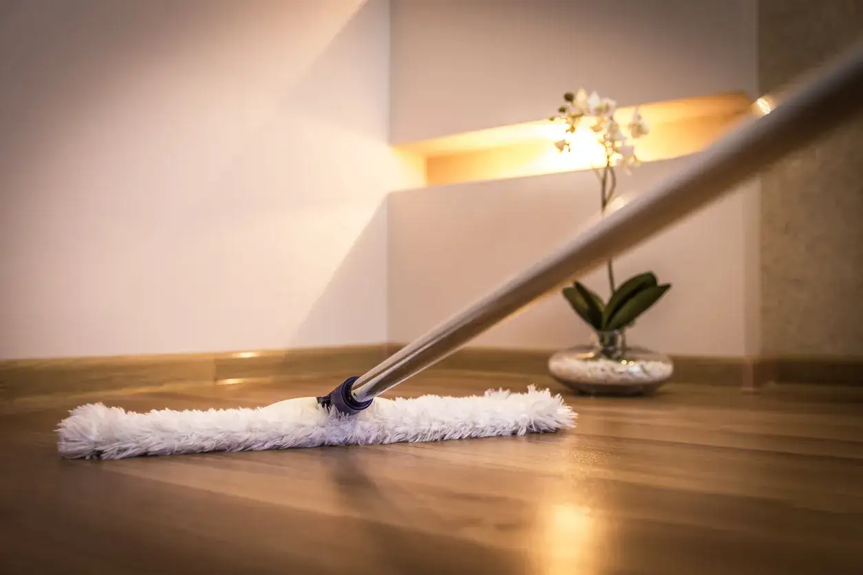 Un mocio in microfibra pulisce un parquet lucido. Un'orchidea in vaso sullo sfondo aggiunge un tocco di eleganza.