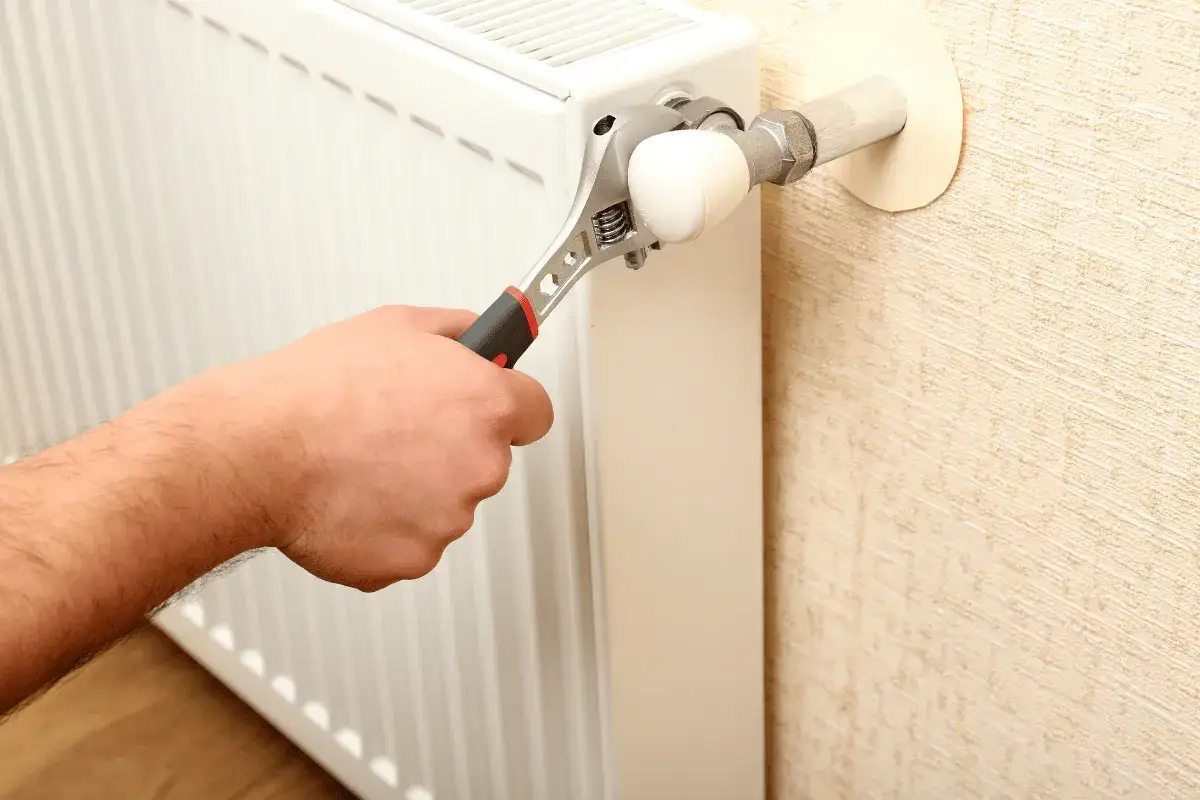 Mano con chiave inglese che agisce sulla valvola di un termosifone bianco, per imparare come svuotare termosifone.