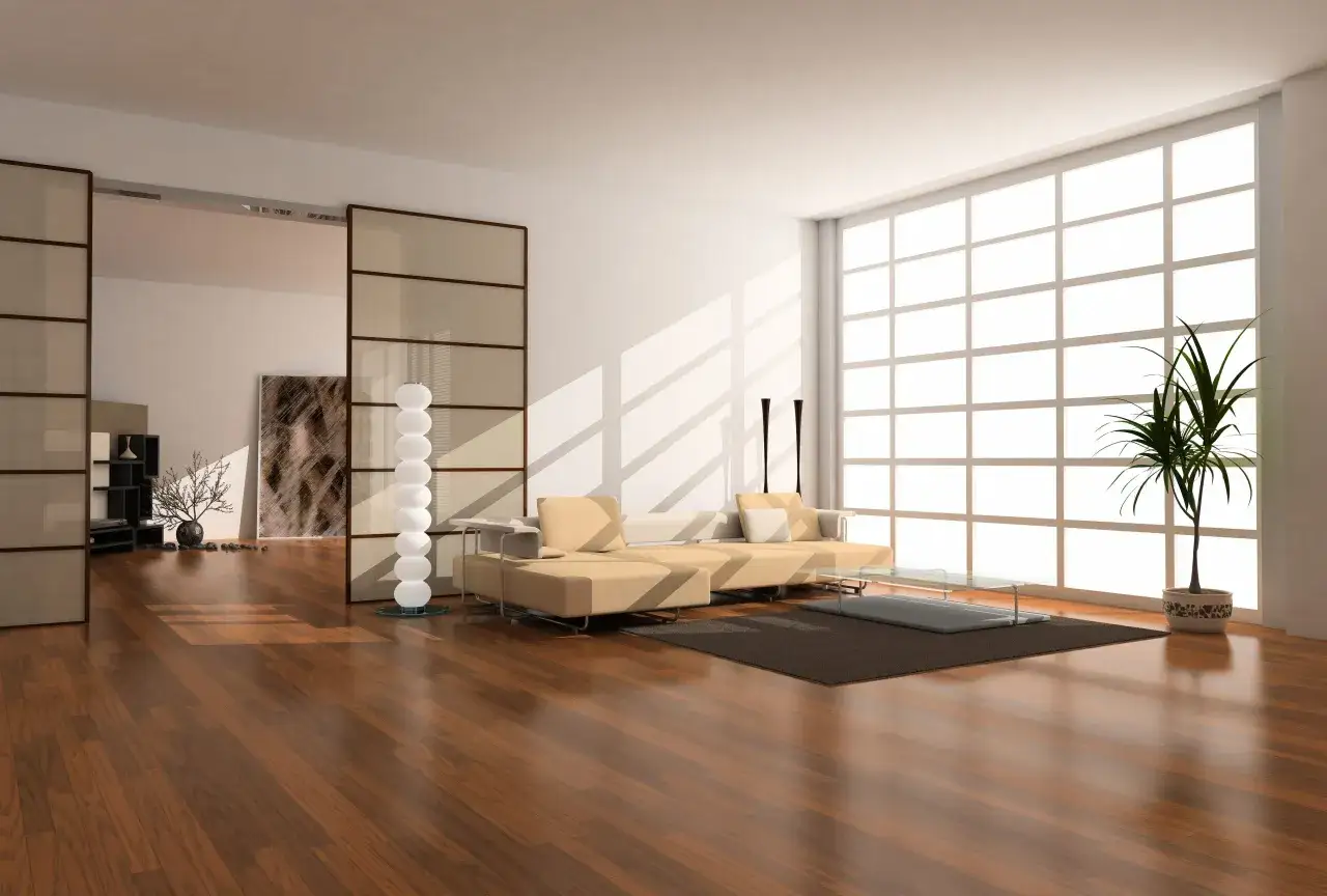 Soggiorno con parquet doussi&eacute; e arredamento moderno. Divano beige, tavolino in vetro, libreria e pianta verde.