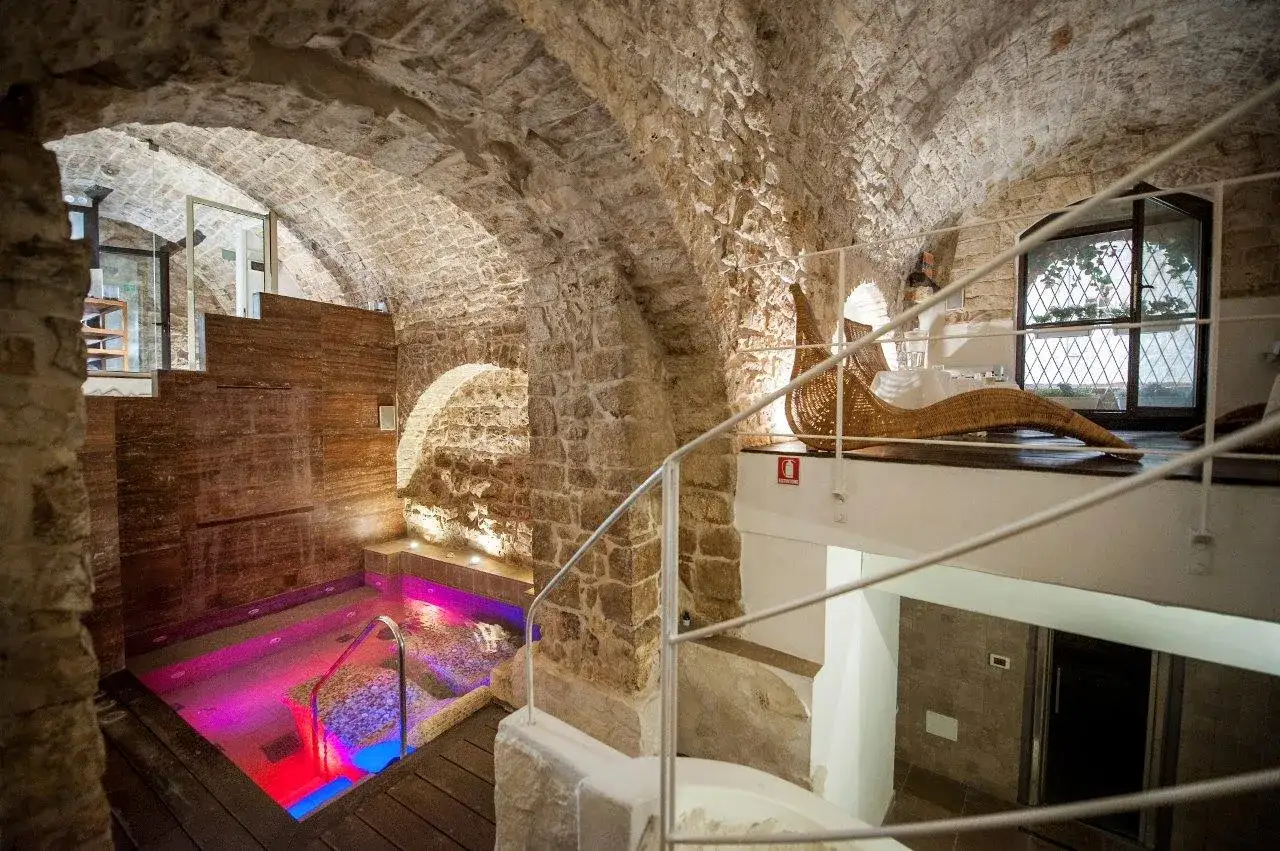 Un'oasi di relax: una vasca idromassaggio con luci colorate, archi in pietra e una zona relax con lettino in vimini. Ecco cos'è un thermarium.