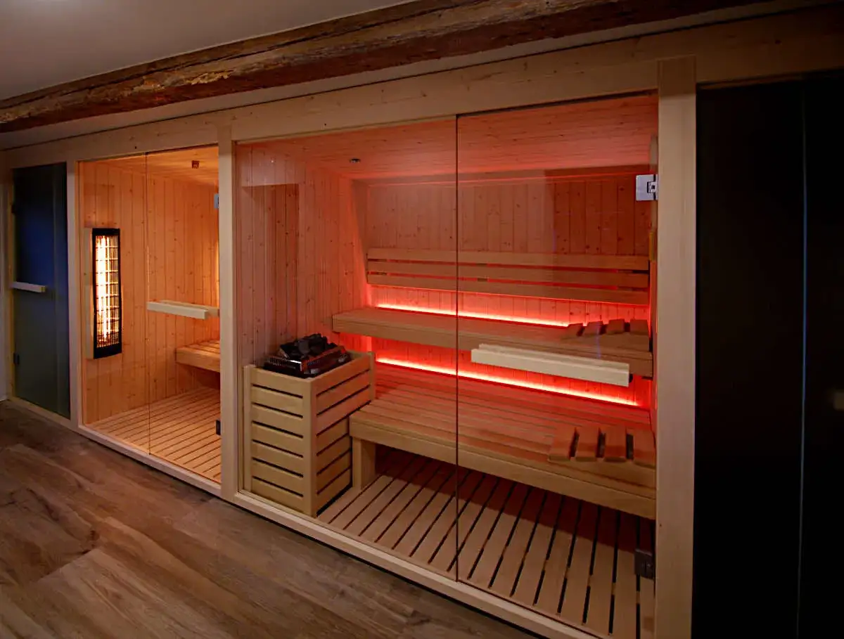 Interno di una moderna sauna in legno con panche, illuminazione rossa e stufa.