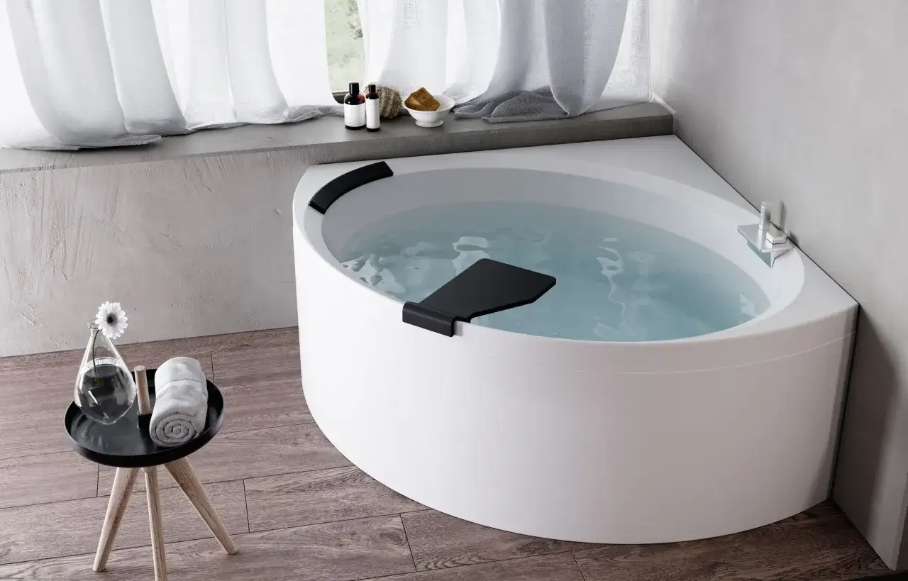 Una vasca da bagno angolare bianca, piena d'acqua, con accessori da bagno e una tenda bianca. Un'esperienza novellini divina.