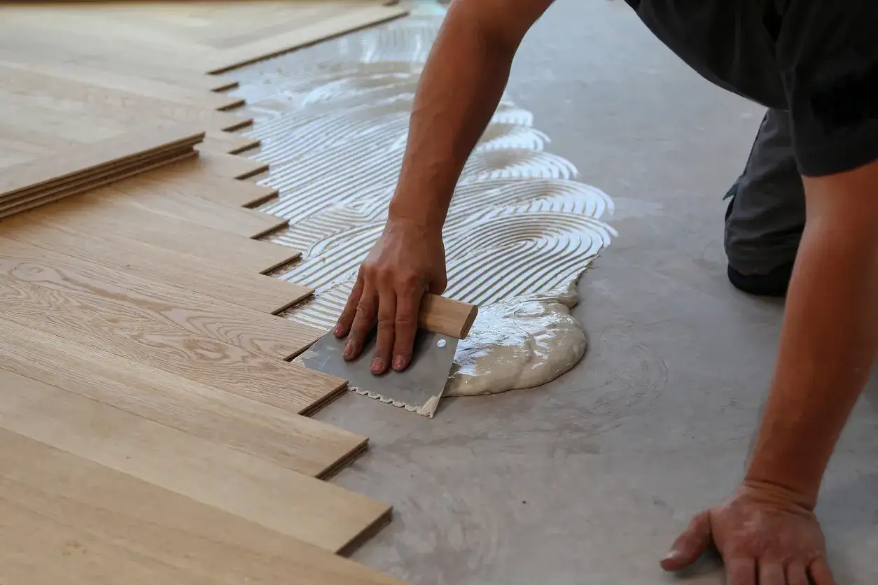Installazione di parquet incollato: stesura colla con spatola dentata su massetto, pronto per posare le tavole di legno.