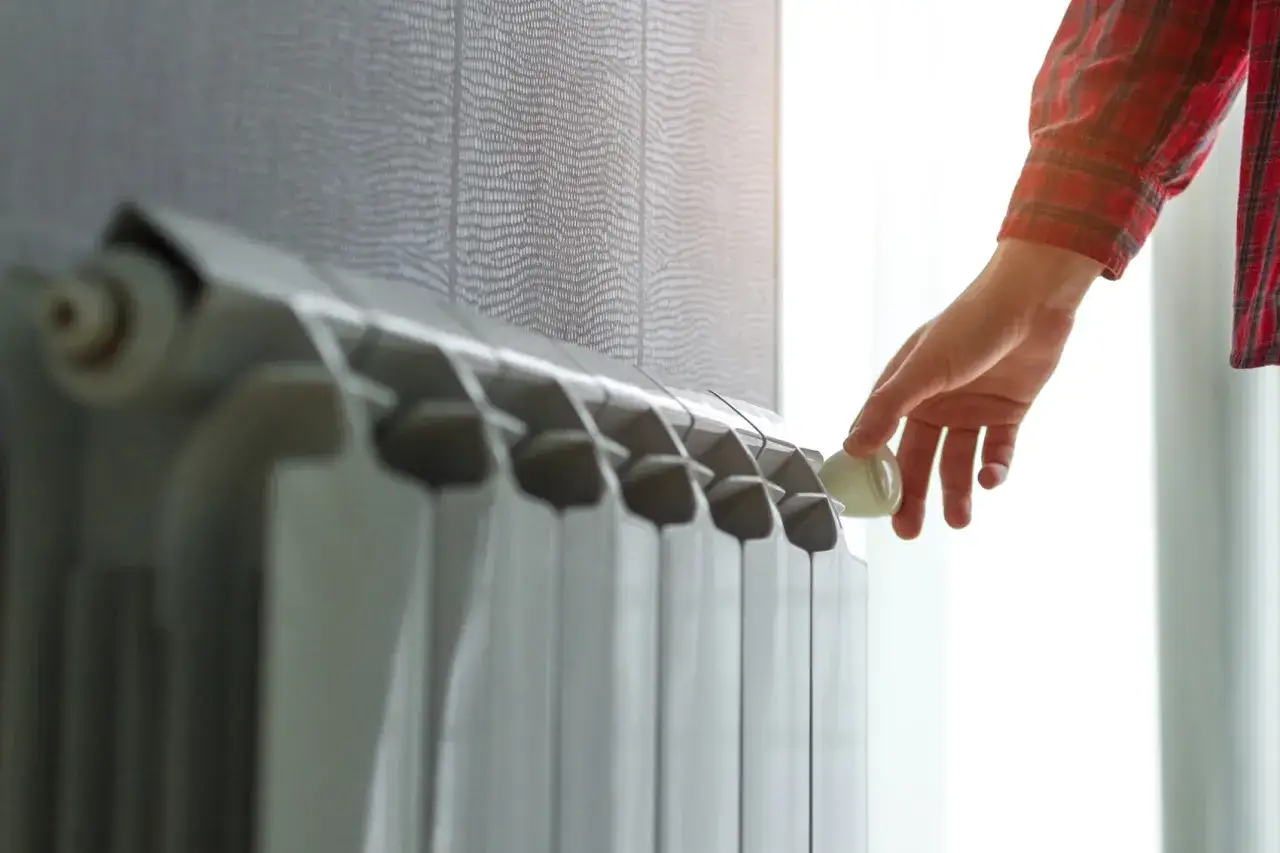 Mano che regola la valvola di un termosifone. Scopri quanto costa cambiare i termosifoni per un riscaldamento efficiente.