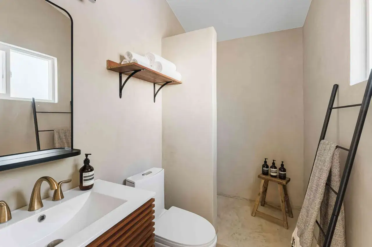 Bagno moderno con lavabo, WC e una zona doccia o aperta o chiusa. Asciugamani arrotolati su una mensola.