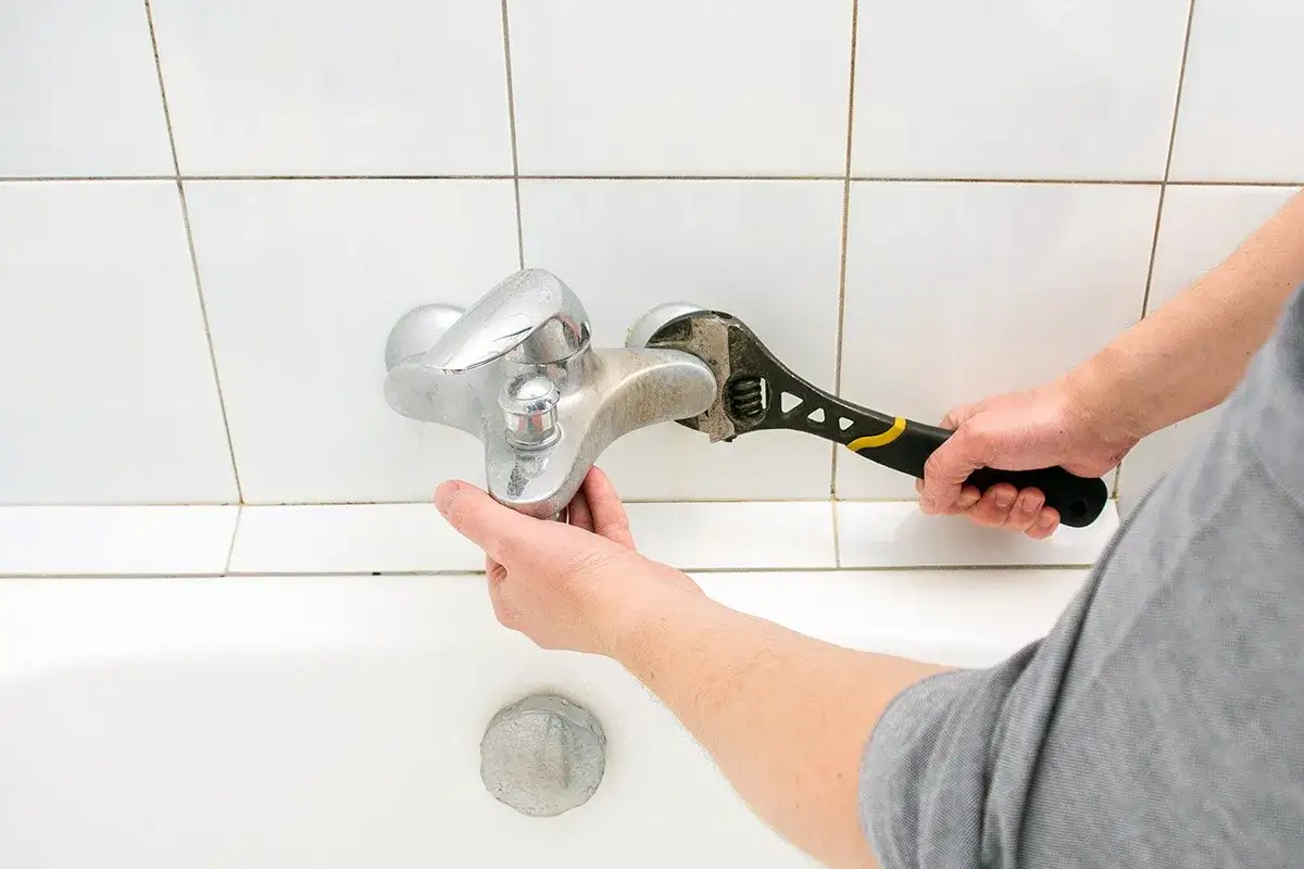 Mano con chiave inglese ripara un rubinetto che perde dal miscelatore, sopra la vasca da bagno.
