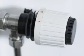 Dettaglio di un detentore termosifone con ghiera bianca e nera, impostato su una tacca intermedia, indica la regolazione della temperatura.