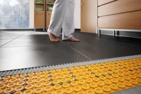Piedi nudi su pavimento scuro, con sistema di riscaldamento a pavimento su pavimento esistente visibile sotto.