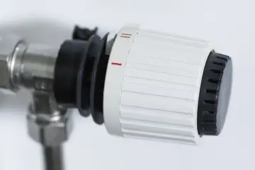 Dettaglio di un detentore termosifone con ghiera bianca e nera, impostato su una tacca intermedia, indica la regolazione della temperatura.