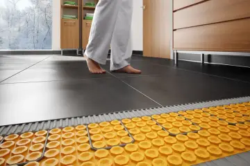 Piedi nudi su pavimento scuro, con sistema di riscaldamento a pavimento su pavimento esistente visibile sotto.