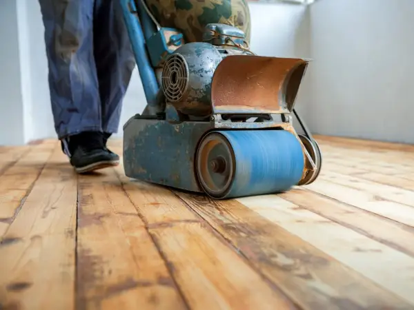 Levigatura parquet: un operaio usa una levigatrice per preparare il pavimento prima dell'imbiancatura. Il legno grezzo risplende sotto la macchina.