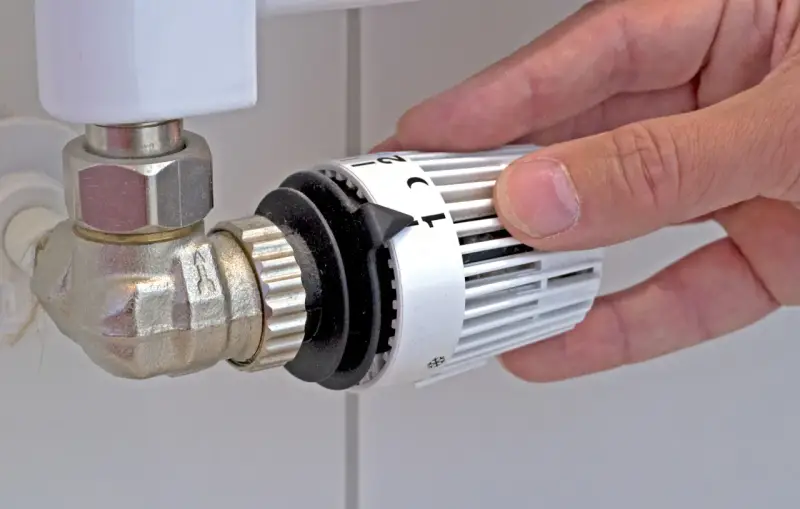 Mano che regola la manopola del termostato per misurare la temperatura dei termosifoni.