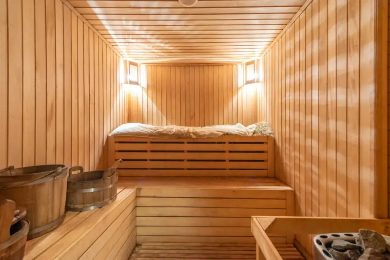 Interno di una sauna norvegese in legno, con panche, secchi e luci soffuse.